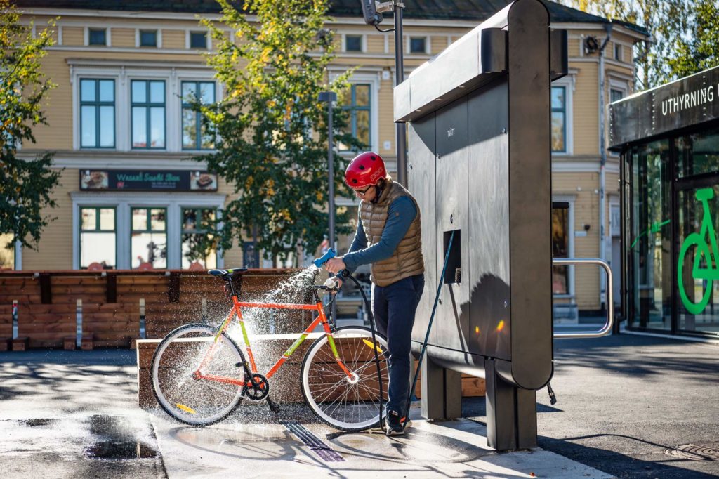 Cyklist i röd hjälm spolar av sin cykel med cykelservicestationen GRAND från Cyklos